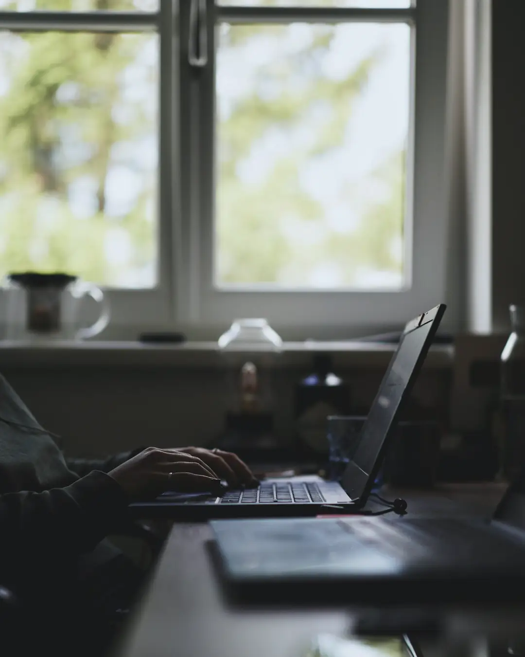 A laptop on a desk beside a window in early morning light
